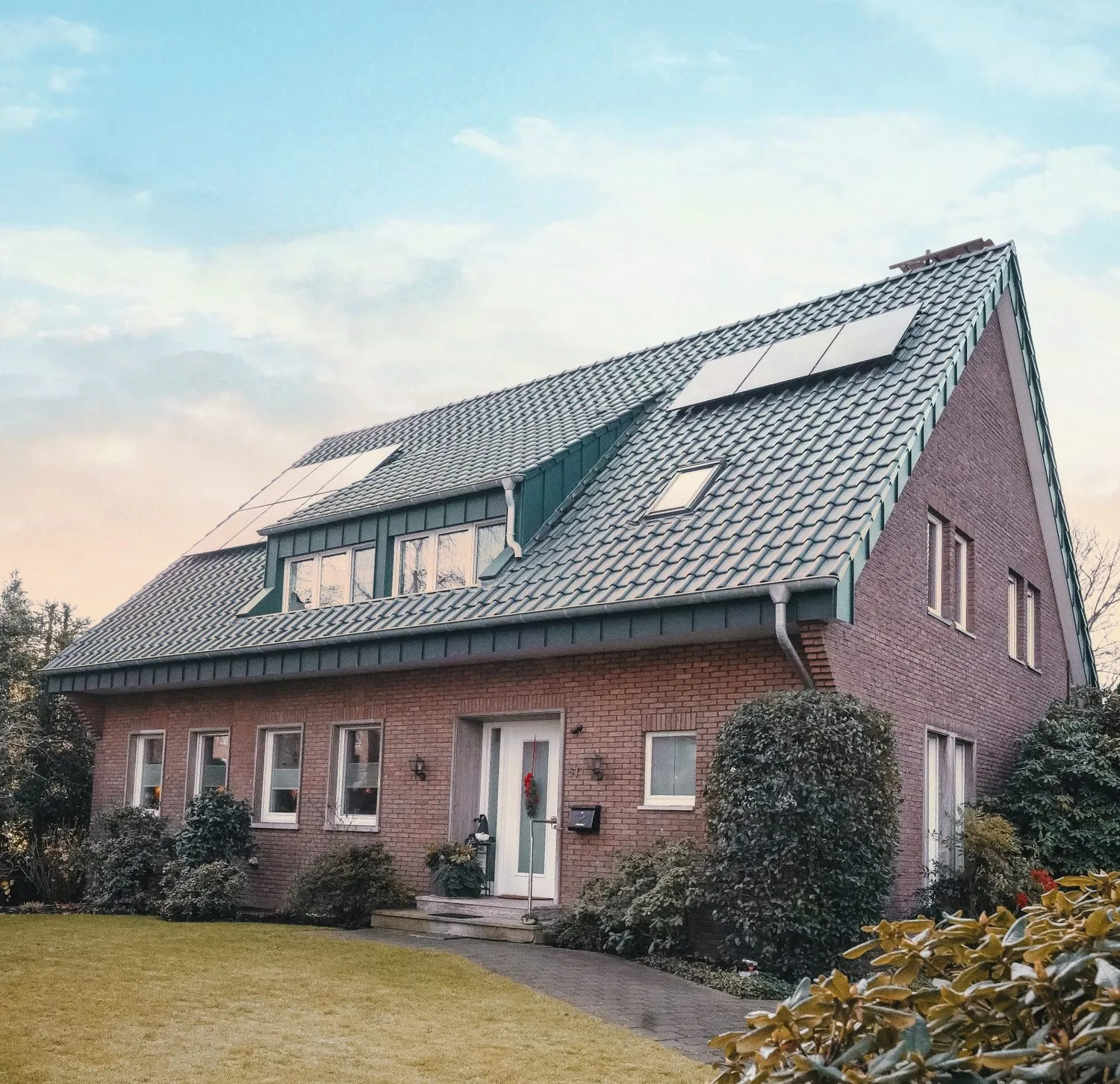 Backsteinhaus mit grün eingedecktem Dach und Dachfenstern