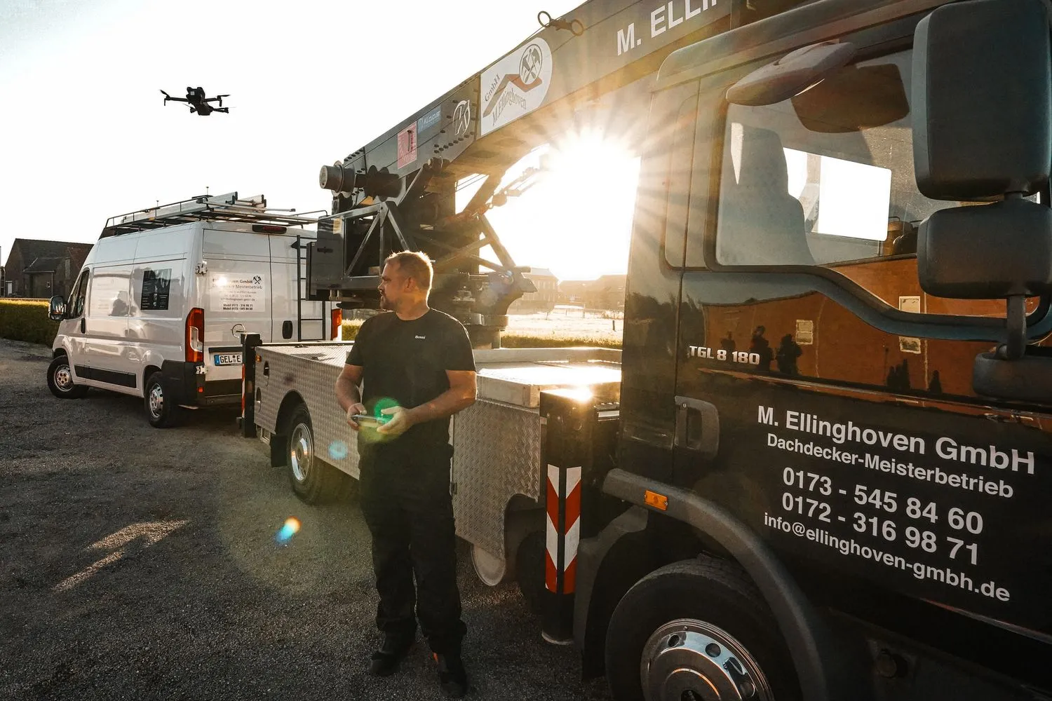 Mitarbeiter mit Drohnen-Fernsteuerung vor dem Kran-Lkw im Gegenlicht